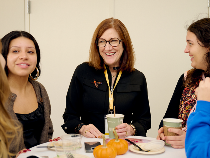 faculty member at a table, in conversation with students