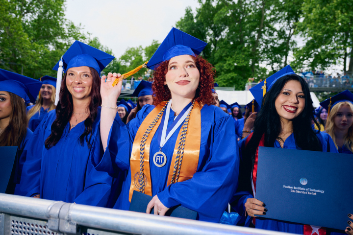 Three students in blue regalia stand at commencement
