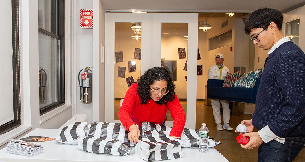 woman at the table wrapping and packing items in a wide striped black and white papar, a man stands next to the table observing