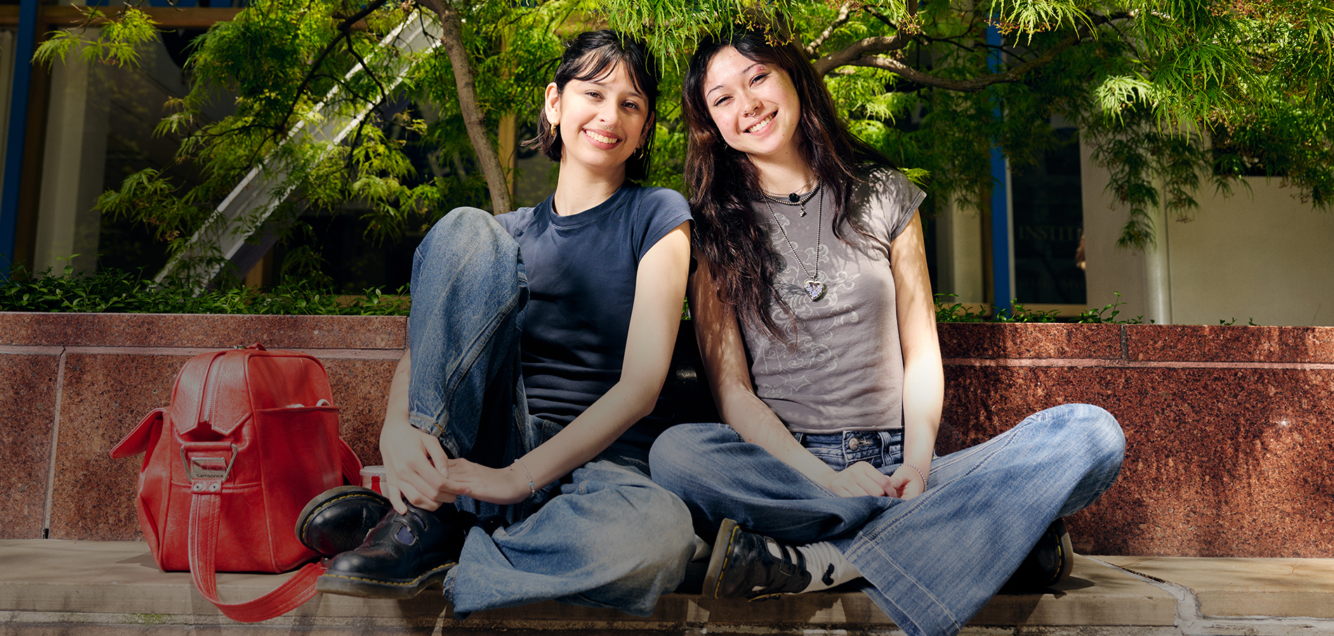 Two smiling FIT students sitting under a tree on campus
