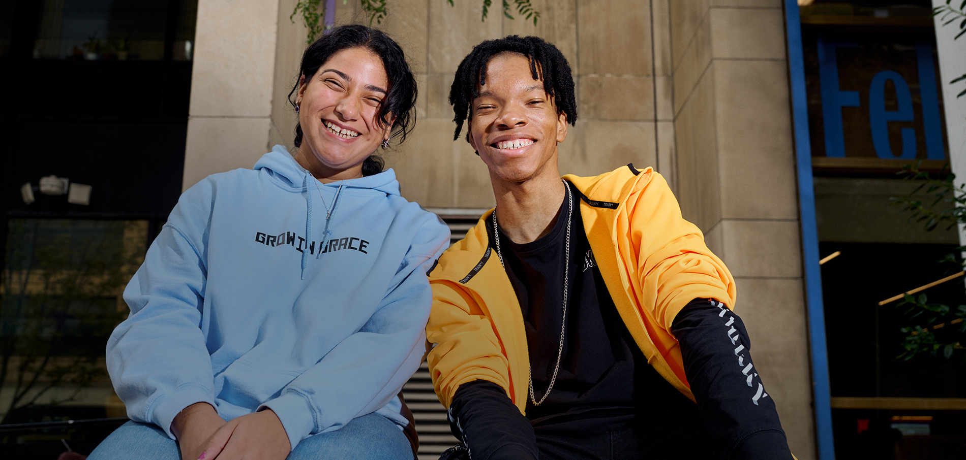 Two smiling FIT students sitting in front of Feldman Center on campus