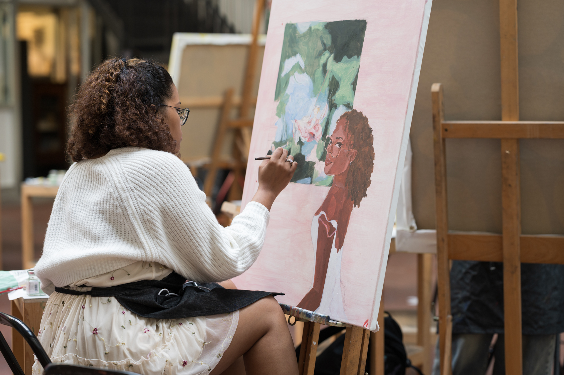 A student paints a portrait in a studio, focused on her colorful canvas.          Ask ChatGPT