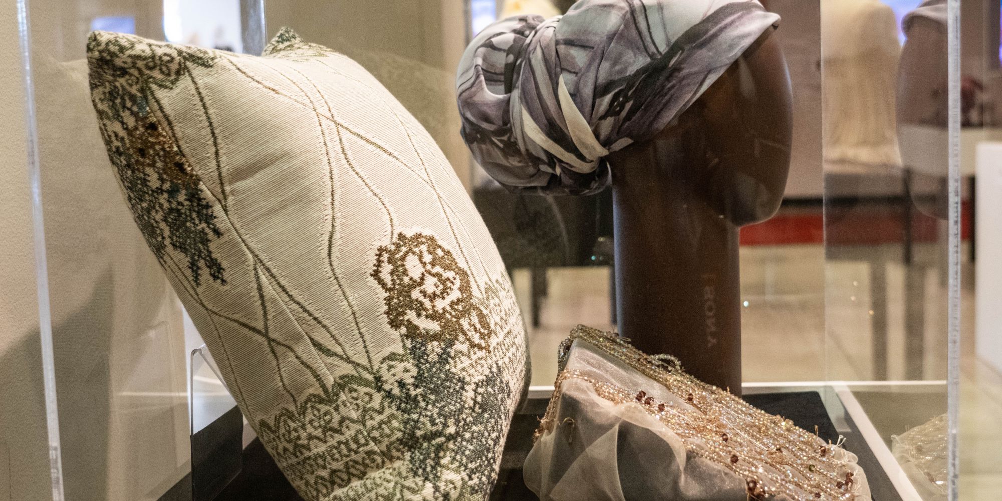Three examples of textile/surface design, a decorative pillow, a sheer fabrick with a beaded geometric design, and a headdress wrap. All items use light backgrounds with earth toned designs