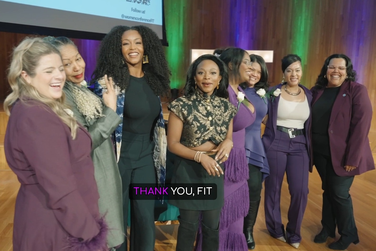 frame from conference video: a group of smiling women with linked arms on stage