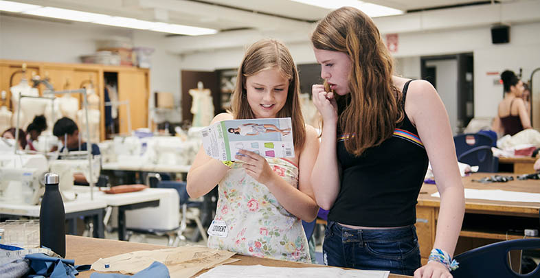 Two students in a sewing room, looking at a pattern