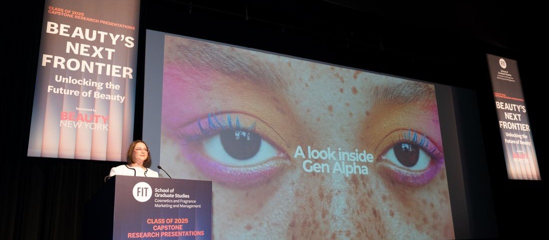 presentation stage with a person at the podium, and large projected image of the person's eyes, brown eyes made up in shades of pink and peachy orange. event banners flanking the projection. They read "beauty's next frontier" 
