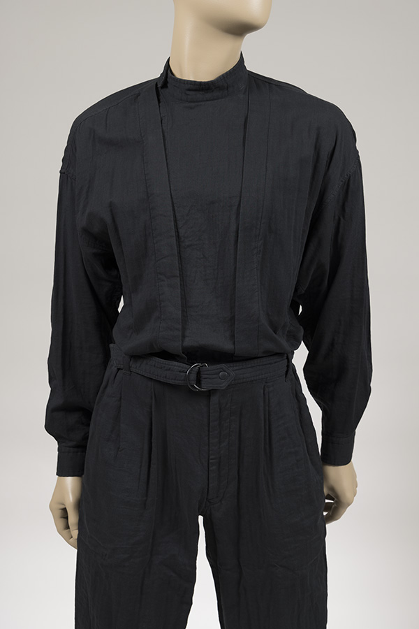 Issey Miyake Men’s black cotton jumpsuit; flight suit styling with band collar, long shirt sleeves, double chest placket with concealed buttons, set-in waistband with a belt and metal d-ring, and tapered legs.