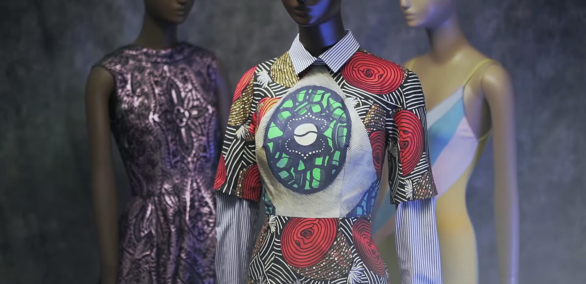 mannequins wearing dresses. from left to right: B. Michael metallic purple silk brocade dress, Stella Jean multipatterned dress, Stephen Burrows color blocked pastel slip style evening dress