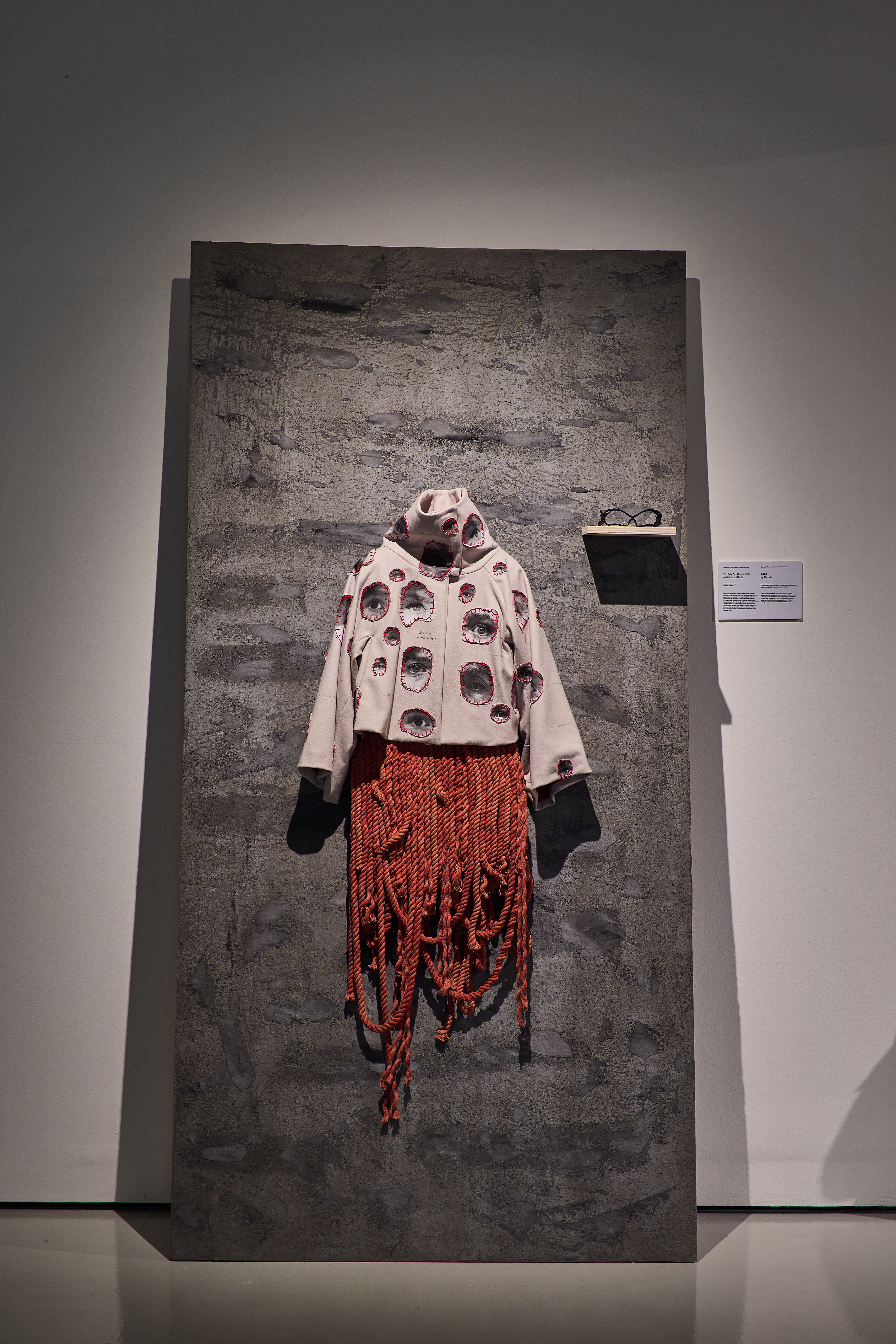 grey sweater with patched, printed images of eyes styled over a red dyed-rope dress
