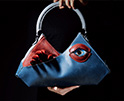 blue handbag with protuding fingers and an eye framed by red lips on front
