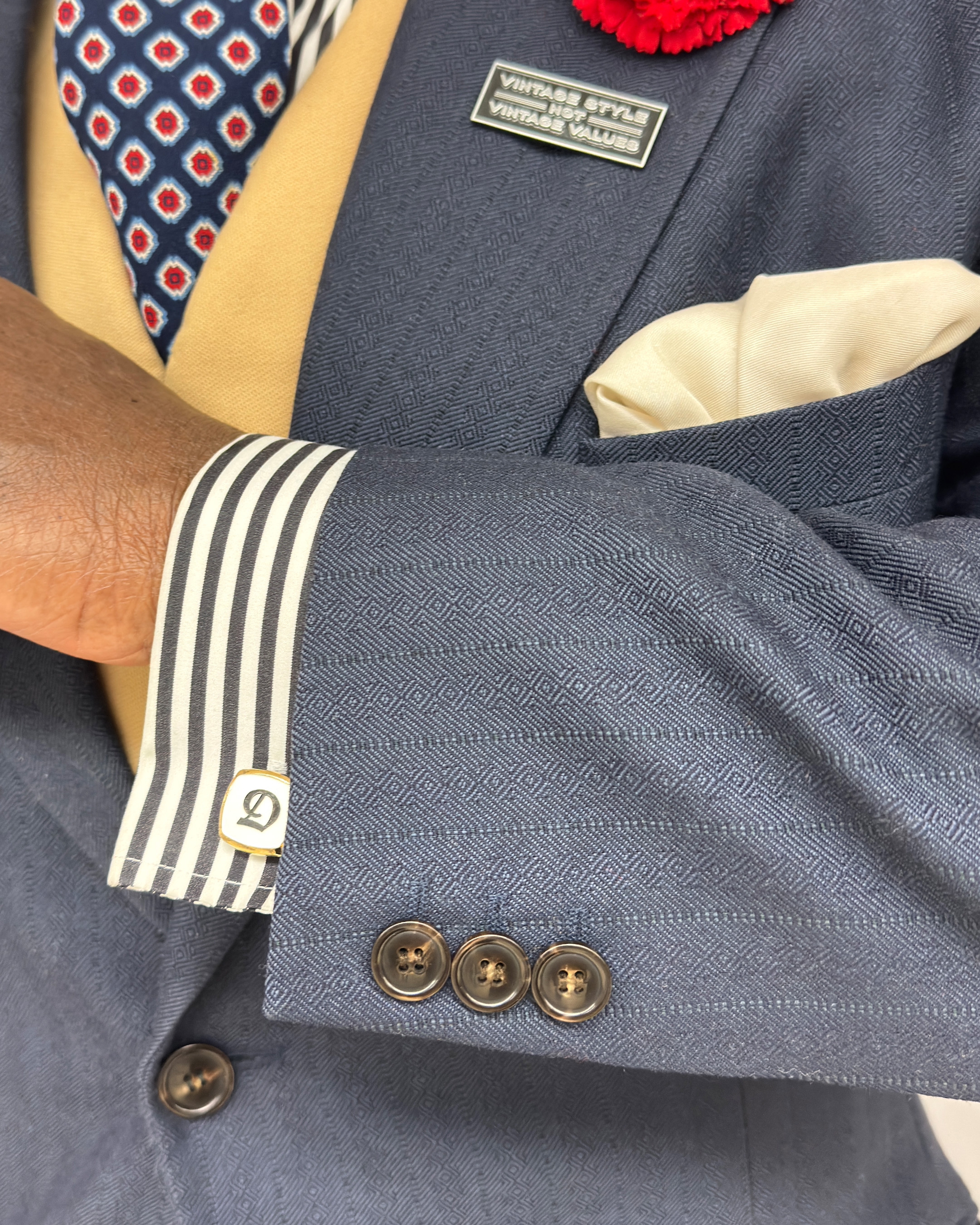 Detail of Dandy's vintage white cuffling with a blue letter D on a white cuff with blue stripes underneath a navy suit jacket