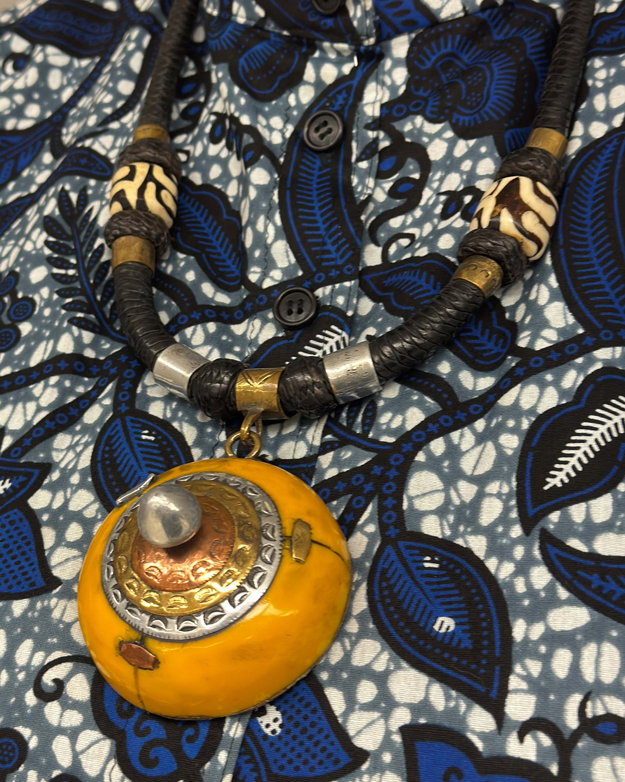 detail of black braided cord necklace with brass beads and chunky, circular yellow pendant at the center