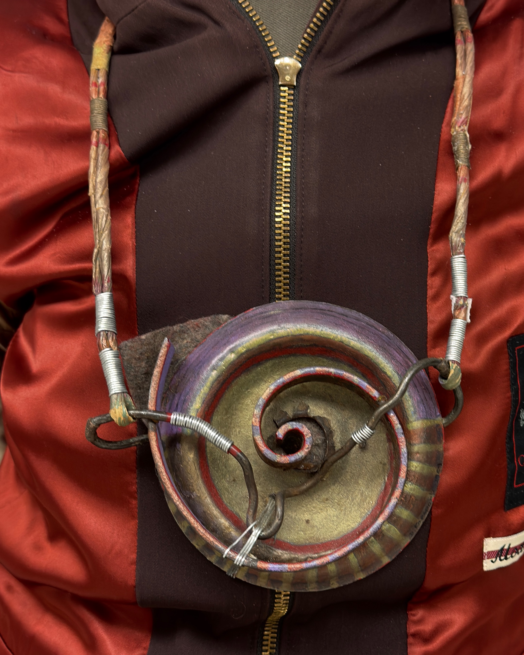 Detail of a circular, metal, patina necklace with swirls