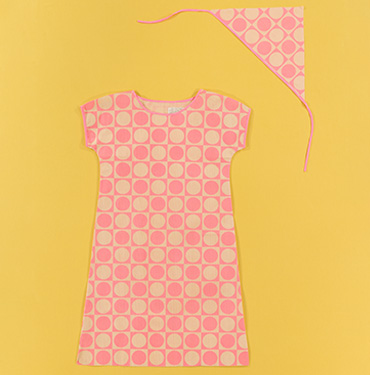 A pink and cream dress with a repeating squircle-and-circle pattern in a checkerboard rhythm, laid flat on a yellow background next to a matching triangular bandana on a stringA pink and cream dress with a repeating squircle-and-circle pattern in a checkerboard rhythm, laid flat on a yellow background next to a matching triangular bandana on a string