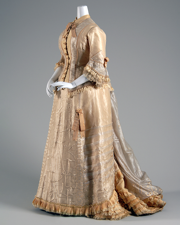 Elegant 18th-century beige silk gown with intricate embroidery, lace trim, and a flowing train displayed on a mannequin