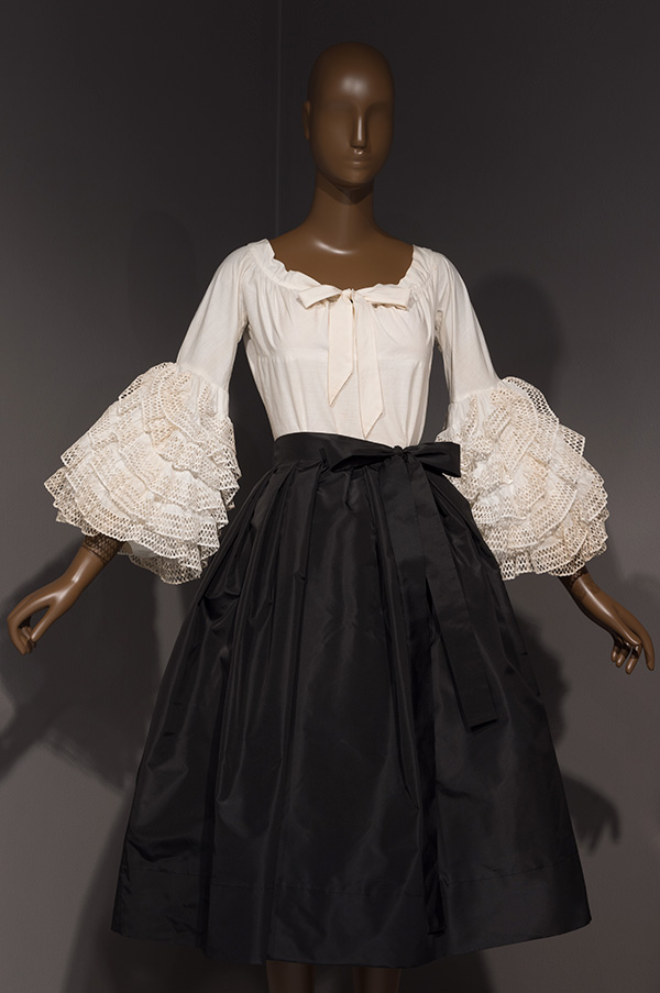 Ruffled tiers of white, lace-trimmed fabric decorate the sleeve of a white cotton blouse.