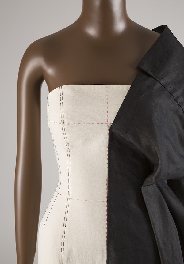 strapless oatmeal colored dress with black and red stitching and black fabric stitched to left side, draped over shoulder